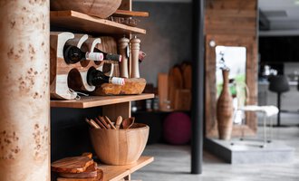 A stylish shelf with wine bottles, wooden dishes, and kitchen utensils. In the background, modern furniture and an appealing room design can be seen. | © Türtscher Die Schreinermanufaktur