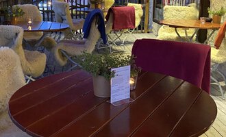 Ein einladender Außenbereich eines Restaurants mit einem runden Tisch und gemütlichen Stühlen. Die Beleuchtung und Umgebung schaffen eine entspannte Atmosphäre am Abend. | © Uusziit | Chantal Kessler