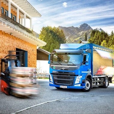 Ein blauer Lkw steht vor einem Holzgebäude mit dem Schriftzug "Walser". Im Hintergrund sind Berge und ein Gabelstapler zu sehen. | © NUFA | Stefan Kothner
