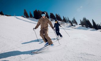 Two skiers are skiing down the slope. The sky is clear and the surroundings are covered in snow. | © Skischule Jörihalde Kleinwalsertal | Ole Zumpolle