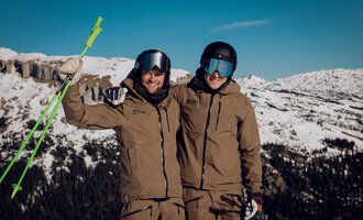 Two skiers are happily posing in the mountains. They are wearing ski clothing and standing in front of a snow-covered landscape. | © Skischule Jörihalde Kleinwalsertal | Ole Zumpolle