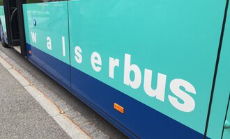 Ein Bus mit der Aufschrift "walserbus" in hellblauer und blauer Farbe. Der Bus steht an einer Station auf einer Straße. | © Kleinwalsertal Tourismus
