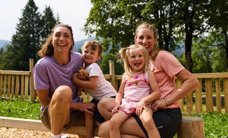 Eine fröhliche Szene mit zwei Erwachsenen und zwei Kindern im Freien. Alle lachen und genießen die Zeit zusammen in der Natur. | © Kleinwalsertal Tourismus | Oliver Farys