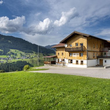 A beautiful wooden house in the mountains with green meadows. The sky is partly cloudy and the landscape appears peaceful. | © Wildentalhütte | Theodor Pinn