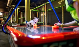 Ein Kind spielt begeistert an einem Air-Hockey-Tisch. Der Raum ist farbenfroh und einladend gestaltet. | © Wonniland Sonthofen | interSPA Gruppe