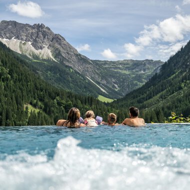 A relaxing pool with people enjoying the view of the mountains and nature. The landscape is green and the mountains are majestic in the background.