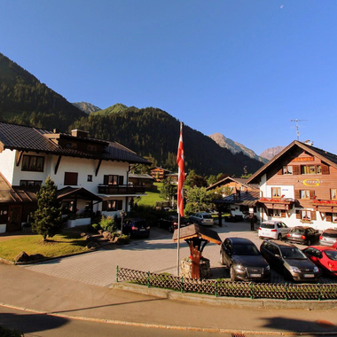 A picturesque building in a mountain landscape with a clear blue sky. Cars are parked in the square in front of the houses.