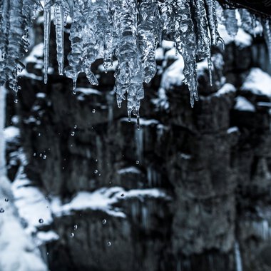 Icicles hanging from a roof over a wintery river in Breitachklamm, with snow falling in the background. | © Kleinwalsertal Tourismus eGen • Photographer: Dominik Berchtold