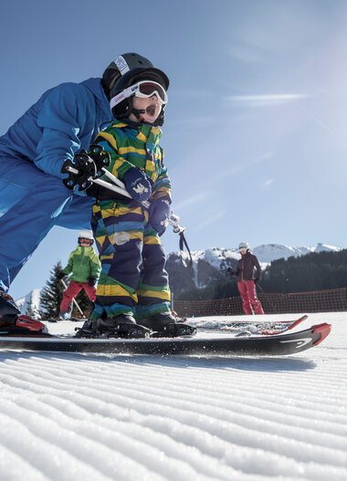 Family skiing on a sunny winter day in the mountains, children learning to ski. | © Kleinwalsertal Tourismus eGen • Photographer: Dominik Berchtold