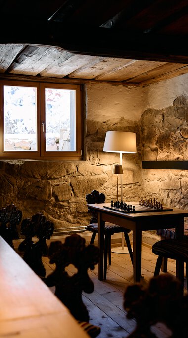 Gemütliches Raum mit Steinaus- und -decke, Tischlampen und einem Schachbrettspiel auf einem Tisch. | © Kleinwalsertal Tourismus eGen • Fotograf: Oliver Farys