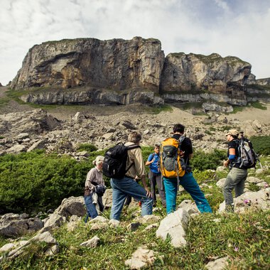 Group of hikers walking in a mountainous landscape with rocks and green grass. | © Kleinwalsertal Tourismus eGen • Photographer: Oliver Farys