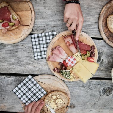 Breakfast table with bread, cheese, cold cuts, and drinks on a wooden surface during a hike in Kleinwalsertal. | © Kleinwalsertal Tourismus eGen • Photographer: Oliver Farys