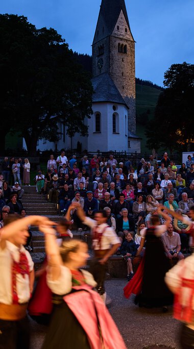 Bilder von einer Trachtengruppe beim Alpenzauber Festival im Kleinwalsertal mit tanzenden Jugendlichen im traditionellen Gewand während der Dämmerung. | © Kleinwalsertal Tourismus eGen • Fotograf: Oliver Farys
