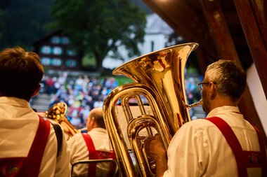 Blasmusik-Ensemble bei einem Auftritt im Freien, mit Blick auf das Publikum im Hintergrund. Die Musiker tragen traditionelle Trachten. | © Kleinwalsertal Tourismus eGen • Fotograf: Oliver Farys