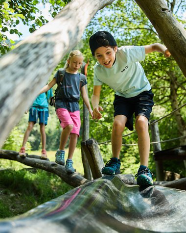Kinder spielen auf einem Holzsteg im Wald, lachen und erkunden die Natur im Kleinwalsertal. | © Kleinwalsertal Tourismus eGen • Fotograf: Oliver Farys