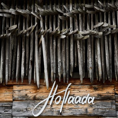 View of a wooden wall with a decorative structure made of wooden chips, beneath a wooden plaque with the word 'Hoflaada' written on it. | © Kleinwalsertal Tourismus eGen • Photographer: Oliver Farys