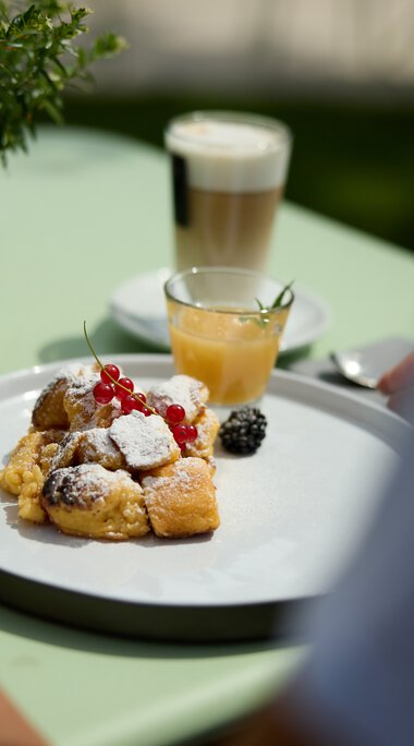 A plate with assorted breakfast pastries, fresh berries, and powdered sugar on a green table during a culinary hike in Kleinwalsertal. | © Kleinwalsertal Tourismus eGen • Photographer: Oliver Farys