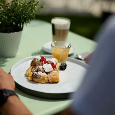 Ein Teller mit verschiedenen Frühstücksgebäcken, frischen Beeren und Puderzucker, auf einem grünen Tisch bei einer kulinarischen Wanderung im Kleinwalsertal. | © Kleinwalsertal Tourismus eGen • Fotograf: Oliver Farys