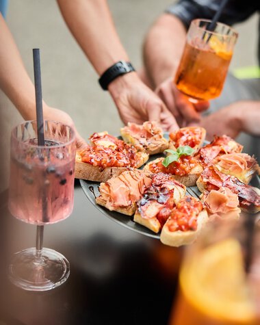 Menschen bei einem Sommer-Event im Kleinwalsertal, die Pizza servieren und Cocktails trinken. | © Kleinwalsertal Tourismus eGen • Fotograf: Oliver Farys