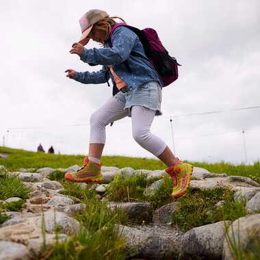 Kind eines Mädchens beim Wandern im Kleinwalsertal, springt über einen Steinweg im Sommer 2025. | © Kleinwalsertal Tourismus eGen • Fotograf: Oliver Farys