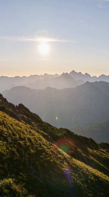 Landschaft im Kleinwalsertal bei Sonnenuntergang, mit Berge und grüne Hügel im Vordergrund. | © Kleinwalsertal Tourismus eGen • Fotograf: Oliver Farys