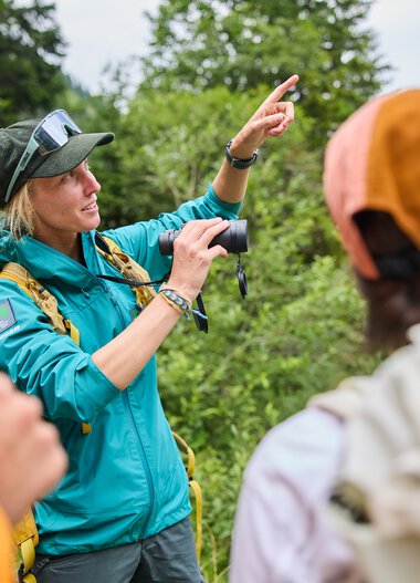 Naturvermittlung im Kleinwalsertal: Ranger erklärt eine Gruppe bei einer Outdoor-Exkursion mit Naturfotografen. Im background sind Bäume und Berge zu sehen. | © Kleinwalsertal Tourismus eGen • Fotograf: Oliver Farys