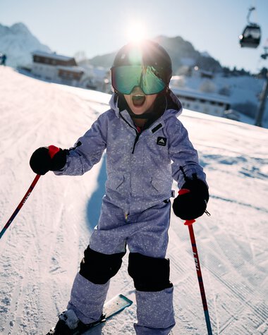 Kleines Kind beim Skifahren auf einer Piste im Snowboard- und Skigebiet im Kleinwalsertal, umgeben von Bergen, mit Skiern und -stöcken, trägt Skibrille und Winterkleidung. | © Kleinwalsertal Tourismus eGen • Fotograf: Oliver Farys