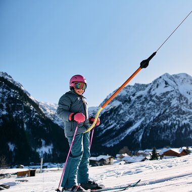 A child skiing in winter with snow-covered mountains and clear sky in the background | © Kleinwalsertal Tourismus eGen • Photographer: Oliver Farys