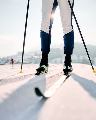 Skifahrer auf der Schwarzwasserloipe beim klassischen Langlaufen im Kleinwalsertal. Spuren im Schnee, Berge im Hintergrund, sonniger Himmel. | © Kleinwalsertal Tourismus eGen • Fotograf: Oliver Farys