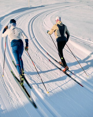 Two cross-country skiers in classic style on a snow-covered trail in Kleinwalsertal, Schwarzwasserloipe, during the winter 2025 season. | © Kleinwalsertal Tourismus eGen • Photographer: Oliver Farys