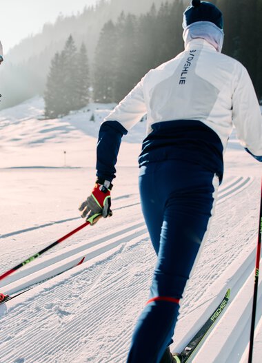 Zwei Skifahrer beim Langlauf auf der Schwarzwasserloipe im Kleinwalsertal, umgeben von verschneiten Landschaften und Bergen. | © Kleinwalsertal Tourismus eGen • Fotograf: Oliver Farys