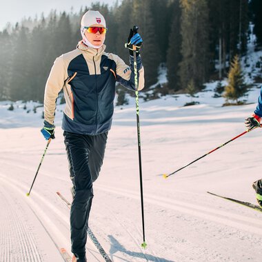 Cross-country skiers on the Schwarzwasserloipe trail in Kleinwalsertal, surrounded by snowy mountains and pine forests. | © Kleinwalsertal Tourismus eGen • Photographer: Oliver Farys