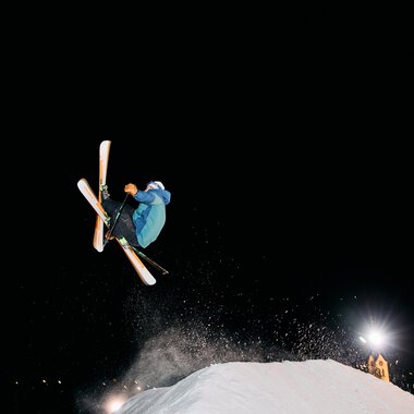 Skier in the air during night skiing in Kleinwalsertal, with a skier performing jumps against the dark night sky. | © Kleinwalsertal Tourismus eGen • Photographer: Oliver Farys