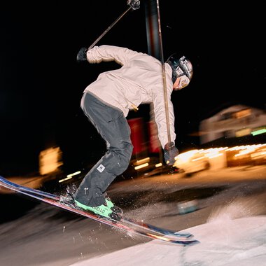 Skier skier night skiing night in Kleinwalsertal under floodlights with motion blur and mountain scenery in the background. | © Kleinwalsertal Tourismus eGen • Photographer: Oliver Farys
