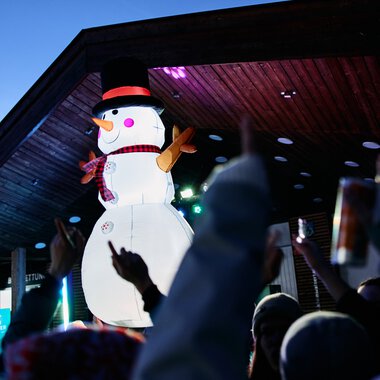 Large snowman decoration at a winter festival in Kleinwalsertal with audience and lights in the background. | © Kleinwalsertal Tourismus eGen • Photographer: Oliver Farys