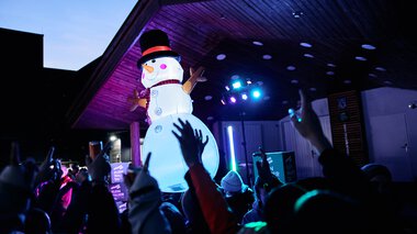 Large inflatable snowman on stage at an event in Kleinwalsertal, with audience and colorful lights. | © Kleinwalsertal Tourismus eGen • Photographer: Oliver Farys