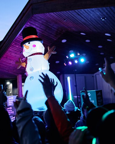 Large inflatable snowman on stage at an event in Kleinwalsertal, with audience and colorful lights. | © Kleinwalsertal Tourismus eGen • Photographer: Oliver Farys