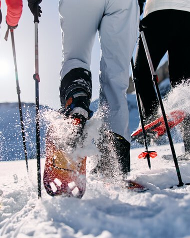 People snowshoeing in the snow, close-up of ski boots and poles in winter. | © Kleinwalsertal Tourismus eGen • Photographer: Oliver Farys