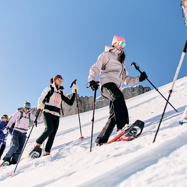 Mehrere Personen bei einer Schneeschuhwanderung im verschneiten Gebirge, unterwegs in winterlicher Kleidung mit Skistöcken. | © Kleinwalsertal Tourismus eGen • Fotograf: Oliver Farys