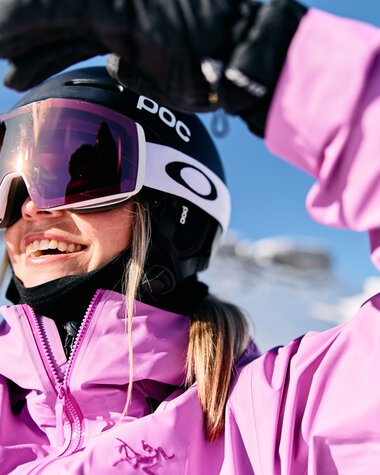 Young woman skiing in winter, wearing pink ski jacket, helmet, and goggles, smiling | © Kleinwalsertal Tourismus eGen • Photographer: Oliver Farys