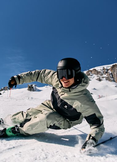 Skier in deep snow with a skier wearing a white ski suit, black helmet, under clear sky at Ski Alpin Ifen. | © Kleinwalsertal Tourismus eGen • Photographer: Oliver Farys