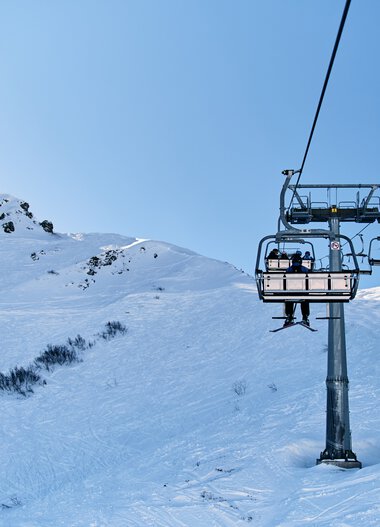 Ski lift in snowy mountain landscape with blue sky at Kleinwalsertal in winter. | © Kleinwalsertal Tourismus eGen • Photographer: Oliver Farys