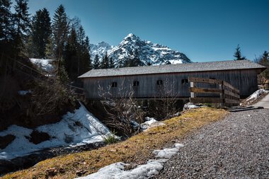 Berglandschaft mit alten Holzwagen und Schneefeldern unter einer klaren blauen Himmel, mit schneebedeckten Gipfeln im Hintergrund. | © Kleinwalsertal Tourismus eGen • Fotograf: Robert Niederwolfsgruber