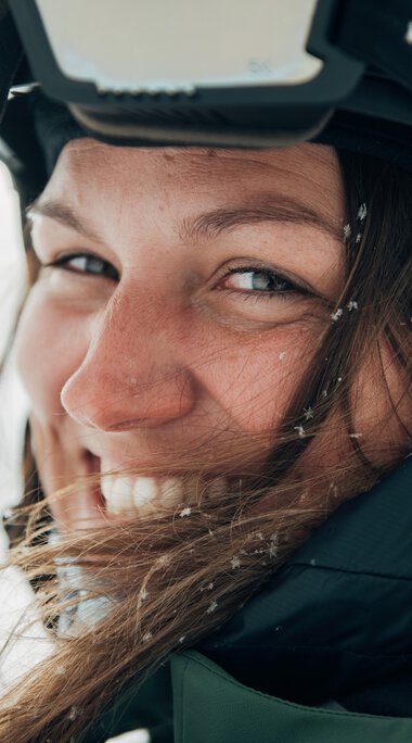 Nahaufnahme einer lachenden Frau mit Skihelm im Schnee, Winteroutfit, bei einem Wintersportshooting. | © Kleinwalsertal Tourismus eGen • Fotograf: Stefan Klauser 