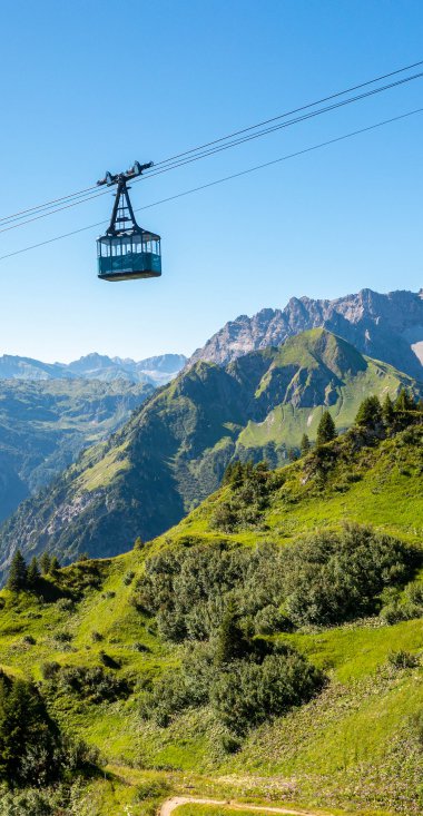 Cable car over green slopes and mountains in Kleinwalsertal under a clear blue sky. | © Oberstdorf · Kleinwalsertal Bergbahnen