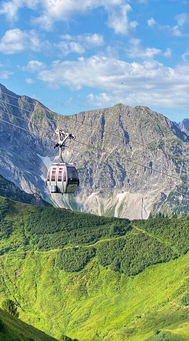 Sommerliche Kanzelwandbahn mit Gondeln im Alpenpanorama, grüne Hügel, Berge und blauer Himmel. | © Oberstdorf · Kleinwalsertal Bergbahnen
