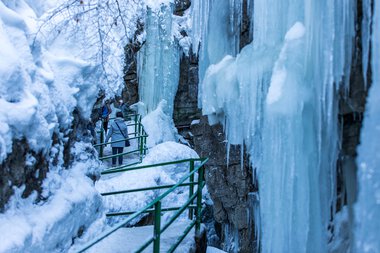 Winter scene at Breitachklamm with frozen water and people exploring the icy landscape along a stepped walkway. | © Kleinwalsertal Tourismus eGen • Breitachklamm • Photographer: Frank Drechsel