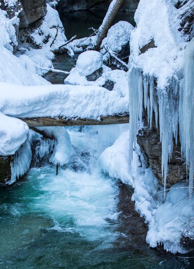 Stream in Breitachklamm during winter, surrounded by frozen water and snow, with ice-covered rocks and icicles. | © Kleinwalsertal Tourismus eGen • Breitachklamm • Photographer: Frank Drechsel