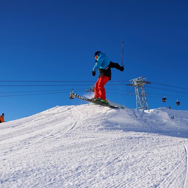 Skier jumps on a snowy mountain during a ski vacation, with a blue sky in the background. | © Kleinwalsertal Tourismus eGen • Oberstdorf Kleinwalsertal Bergbahnen