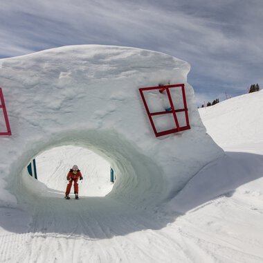 Large snow sculpture of a head with red windows, in the Oberstdorf/Kleinwalsertal ski area, with a skier underneath. | © Kleinwalsertal Tourismus eGen • Oberstdorf Kleinwalsertal Bergbahnen